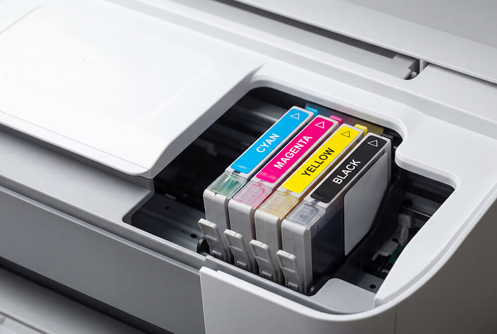 Cyan, magenta, yellow, and black replacement ink cartridges installed inside an open inkjet printer.