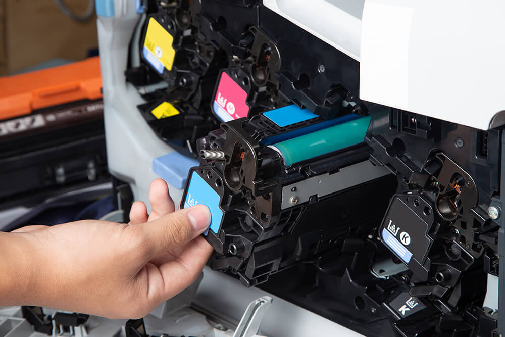 Hand installing a blue laser toner cartridge into a colour laser printer.